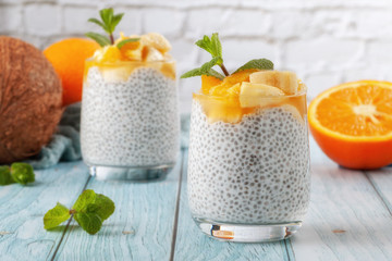 Fototapeta na wymiar Chia pudding with banana in two glass glasses with raw chia seeds on a blue wooden table