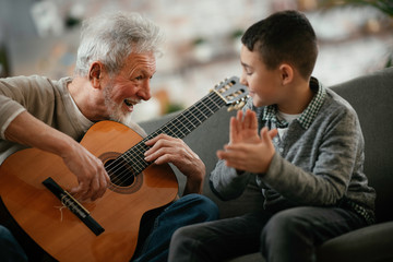 Grandpa and grandson playing guitar. Grandfather and grandson enjoying at home.	
