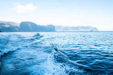 Fototapeta na wymiar Blue sea with prop wash wake and cliffs in horizon at daytime