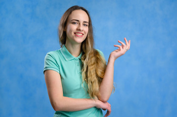 Portrait of a caucasian girl with long hair in a turquoise t-shirt at the camera talking with a smile. Photo taken on a blue background.