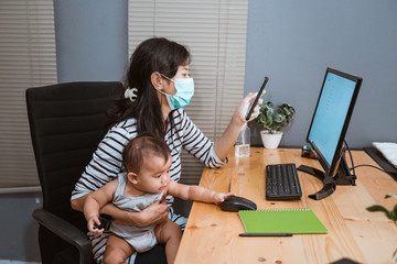 asian working mom wearing masks carrying her baby while working from home office