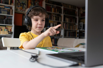 Indoor life at the coronavirus quarantine. Cute curly boy has school lesson online.