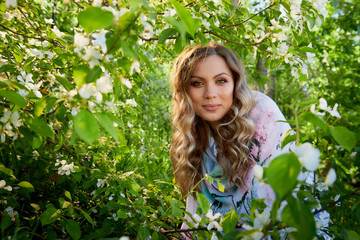 Portrait of a beautiful blonde girl with green eyes and blossoming apple tree with white flower in the park in a spring time