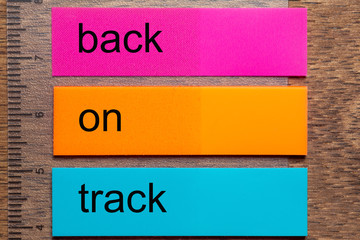 Three bookmark stickers with the words back on track, on a dark natural wooden table