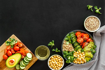 Quinoa, avocado and chickpeas in bowl in hands - balanced healthy food - on black table. Top view copy space