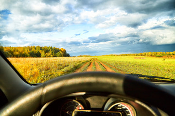 View from car window on beautiful landscape with field and road. Autumn nature with sky full of...