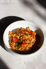 Bulgur casserole in tomato sauce with courgette in a bowl. Bulgur and vegetable bowl. On grey table. Sunlight. 