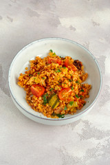 Bulgur casserole in tomato sauce with courgette in a bowl. Bulgur and vegetable bowl. On grey table.