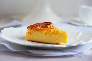 Homemade cheesecake with sliced almonds on plate on grey table. Selective focus, natural light.