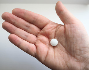 In the right female hand a white round pill on a white background