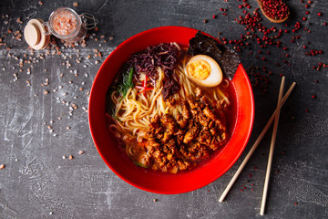 delicious hot japanese ramen noodle soup in red bowl on the grey background with chopsticks, top...