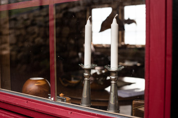 View through the window. Two white candles in metal candleholders standing on window seal