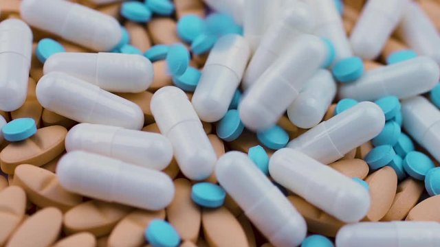 Small blue pills fall on white capsules with antibiotic and orange vitamins.