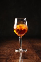 delicious cool dark cocktail with ice in a beautiful unique wine glass on the dark wooden background, side view, vertical