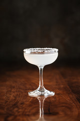 delicious muddy white cocktail in margarita glass with salt at the edges on the dark wooden background, side view, vertical