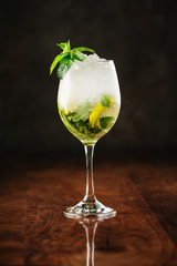 fresh cooling mojito cocktail with min leaves and crushed ice in wine glass on the dark wooden background, vertical, side view