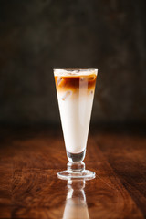 delicious cold chocolate ice cream milkshake with syrup in a long glass, dark wooden background, side view, vertical