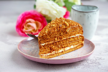 Slice of fresh homemade russian or czech honey cake with cup of tea or coffee on grey table. Selective focus. Natural light.