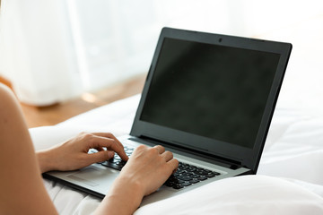 Beautiful asian woman working on a laptop sitting on the bed in the house.Woman checking social apps and working.Work from home concept.