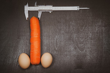 Concept of increasing male penis and operation, increase male organ, carrot with two eggs and a caliper on a black background © evgenii