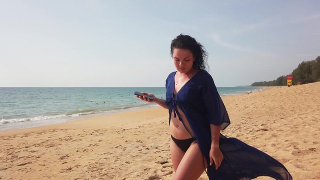 Beautiful brunette walks on a long deserted beach and looks into her phone