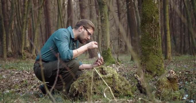 Confident bearded man in eyeglasses taking part of green moss that growing on old tree for discovering features in laboratory. Mature botanist carefully doing his job outdoors.