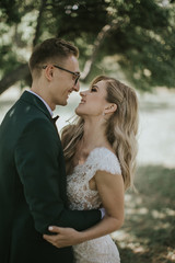 Portrait of a lovely bride and groom embrace, kiss and hug each other. Couple in love in the bosom of nature . Handsome groom and beautiful blonde bride posing in the forest. Modern dress and suit