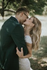 Portrait of a lovely bride and groom embrace, kiss and hug each other. Couple in love in the bosom of nature . Handsome groom and beautiful blonde bride posing in the forest. Modern dress and suit