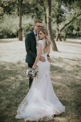 Portrait of a lovely bride and groom embrace, kiss and hug each other. Couple in love in the bosom of nature . Handsome groom and beautiful blonde bride posing in the forest. Modern dress and suit