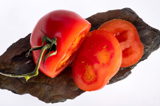 saftige Tomate angeschnitten auf dunklem Stein liegend, geschmackvolle Paradiesfrucht in der gesunden Ern&auml;hrung