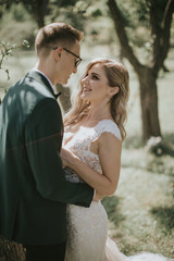 Portrait of a lovely bride and groom embrace, kiss and hug each other. Couple in love in the bosom of nature . Handsome groom and beautiful blonde bride posing in the forest. Modern dress and suit