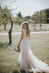 Fototapeta na wymiar Portrait of a wedding bride walking in a white modern hipster dress. Caucasian blonde bride in a vintage dress in the forest on sunset. Attractive lady posing with a bouquet of flowers