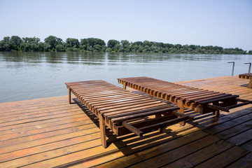 Two wooden sun loungers by the water