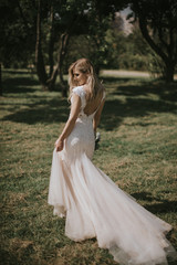 Portrait of a wedding bride walking in a white modern hipster dress. Caucasian blonde bride in a vintage dress in the forest on sunset. Attractive lady posing with a bouquet of flowers