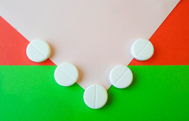 white pills on a red and green background. snow-white round antibiotics against viruses.