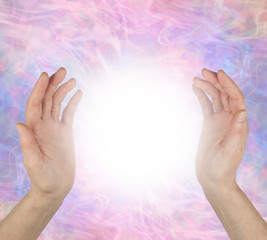 Sensing spiritual healing energy field between hands - female hands 25 cm apart opposite each other with a bright white light orb energy between against a pale pink purple energy field  background 
