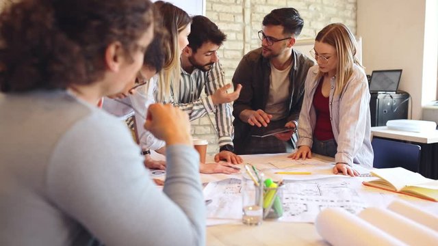 Group of modern business people in casual wear discussing architectural designs while sitting in the creative office.