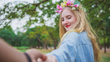 Fototapeta premium Young woman holding man hand leading in public park in vacation