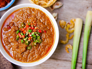 The Siam cuisine concept : top view over bowl of spicy shrimp paste with dry shrimp and blurry lemongrass on wood table show its ingrediants 