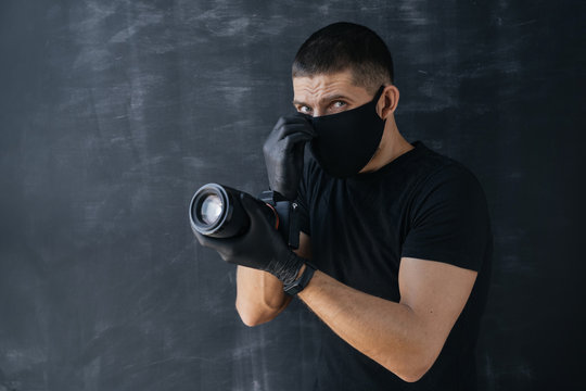 Portrait of a photographer, a man in a black medical mask and gloves, holding a professional digital camera and looking into the frame. Self-isolation and quarantine. Protection.