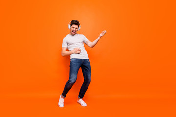 Fototapeta na wymiar Full length photo of funky guy chilling listen modern earphones hold hands play imagine guitar rehearse wear striped t-shirt jeans shoes isolated bright orange color background