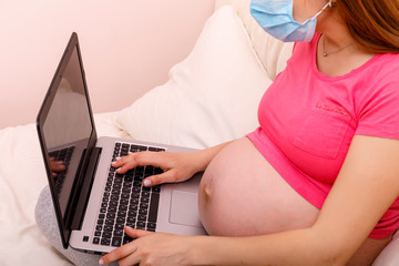 Naklejka premium Beautiful pregnant young woman working on a laptop sitting on the bed in the bedroom. Concept of female business, shopping, home office, quarantine, coronavirus covid 19 ncov. Stay at home concept.