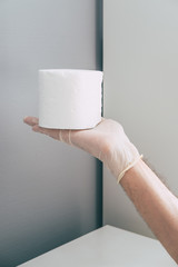 A medical worker in rubber latex gloves on his hands holds toilet paper roll . Concept of coronavirus panic.