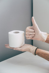 A medical worker in rubber latex glove on his hand holds toilet paper roll and shows Okay or Like sign. Concept of coronavirus panic. Isometric and geometric style in the corner.