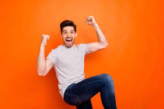 Photo of crazy funky guy yelling loud open mouth raise fists sportive cheerleader rejoicing best win team wear casual striped t-shirt jeans isolated bright orange color background