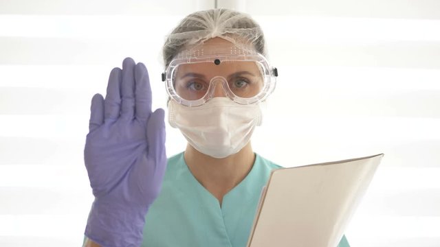 Young nurse or woman doctor in a medical mask, goggles and disposable gloves. She makes a warning gesture.