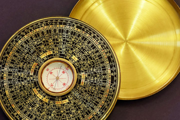 Old vintage chinese compass used in feng shui, golden item with hieroglyphs and cover, on dark brown background. Selective focus, copy space.