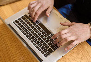 young guy is typing on a computer in a coffee shop, close-up of hands and keyboard