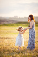 mom hold little daughter in dress jumping in field