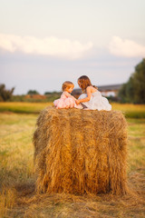 Naklejka na ściany i meble small girls sit on haystack wheat field sunset